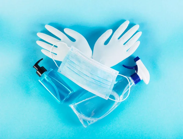 医疗面罩 消毒液 蓝色背景的乳胶手套 心形构图中的冠状病毒保护概念 保护好你自己 准备好验尸吧 图库照片