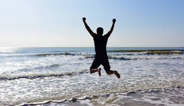 Jumping man above sea water and waves in sunny day.