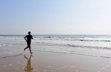 Dalgalar ile sahilde jogging adam.