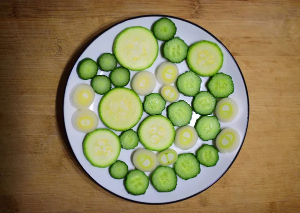 Tranches de concombre et de courge fraîches sur plaque blanche avec fond de bois . — Photo