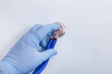 Doktor, açık mavi arka planda steteskoplu mavi eldivenleri teslim et..