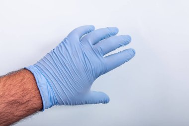 Doktorun eli açık mavi arka planda mavi bir tıbbi eldiven giymiş..