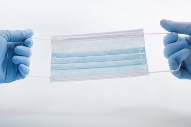 Mavi eldivenli doktor elinde açık mavi arka planda tıbbi koruyucu maskeler tutuyor..
