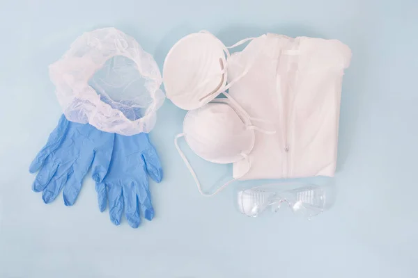 dust mask, blue gloves, protective suit and head cover isolated on a light blue background.