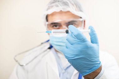Yumuşak odaklı arka planda şırıngası olan beyaz bir doktor görüntüsü.