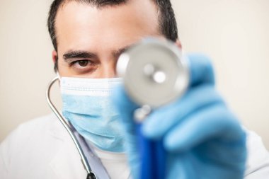 Beyaz arka planda steteskop ve yüz maskesi olan beyaz bir doktor..