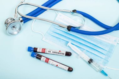 Açık mavi arka planda steteskop, maske ve şırınga ile enfekte olmuş Coronavirus 'lu hayali kan örnekleri..
