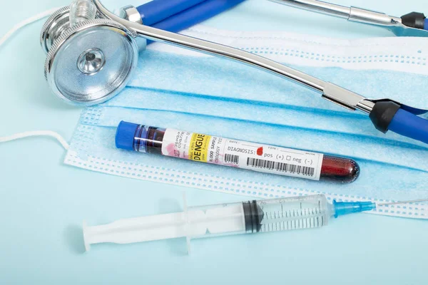 Fictional Blood samples with infected dengue virus, with stethoscope, mask and syringe on a light blue background.