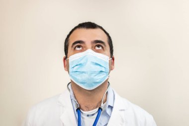 Beyaz bir arka plana bakan, yüz maskesi olan beyaz bir doktor..