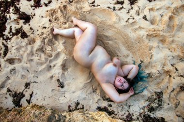 Güzel, şehvetli bir kadın doğada, kumsalın kıyısında çıplak poz veriyor..