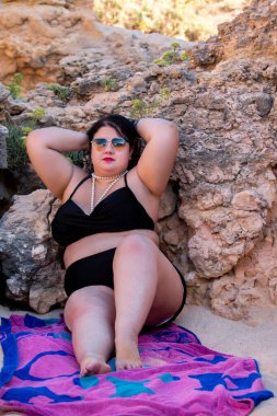 Siyah bikinili ve kumsalda koyu renk güneş gözlüklü güzel, şehvetli bir kadın..