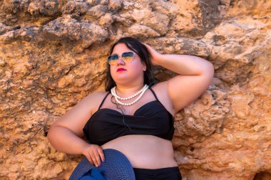 Siyah bikinili ve kumsalda koyu renk güneş gözlüklü güzel, şehvetli bir kadın..