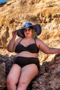 Siyah bikinili ve kumsalda koyu renk güneş gözlüklü güzel, şehvetli bir kadın..