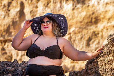 Siyah bikinili ve kumsalda koyu renk güneş gözlüklü güzel, şehvetli bir kadın..