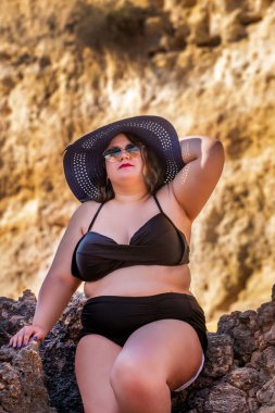 Siyah bikinili ve kumsalda koyu renk güneş gözlüklü güzel, şehvetli bir kadın..