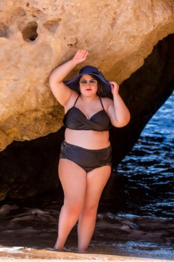 Siyah bikinili ve kumsalda koyu renk güneş gözlüklü güzel, şehvetli bir kadın..