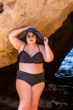 Siyah bikinili ve kumsalda koyu renk güneş gözlüklü güzel, şehvetli bir kadın..