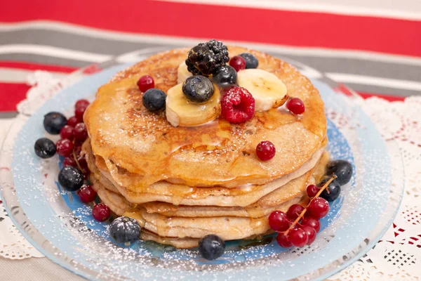 Delicious oats and banana pancakes with mixed berries fruits and sugar powder dripping with honey.