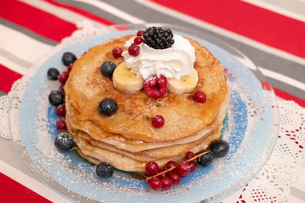 Delicious oats and banana pancakes with mixed berries fruits and sugar powder dripping with honey.
