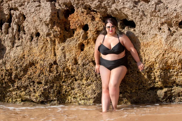 beautiful sensual woman with black bikini and dark shades on the beach.