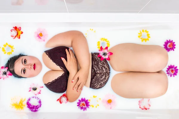 女人穿着性感的红色内衣裤躺在有花的牛奶浴缸里 — 图库照片