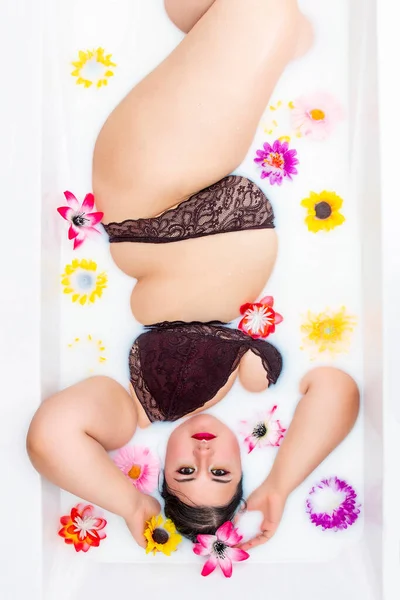 女人穿着性感的红色内衣裤躺在有花的牛奶浴缸里 — 图库照片