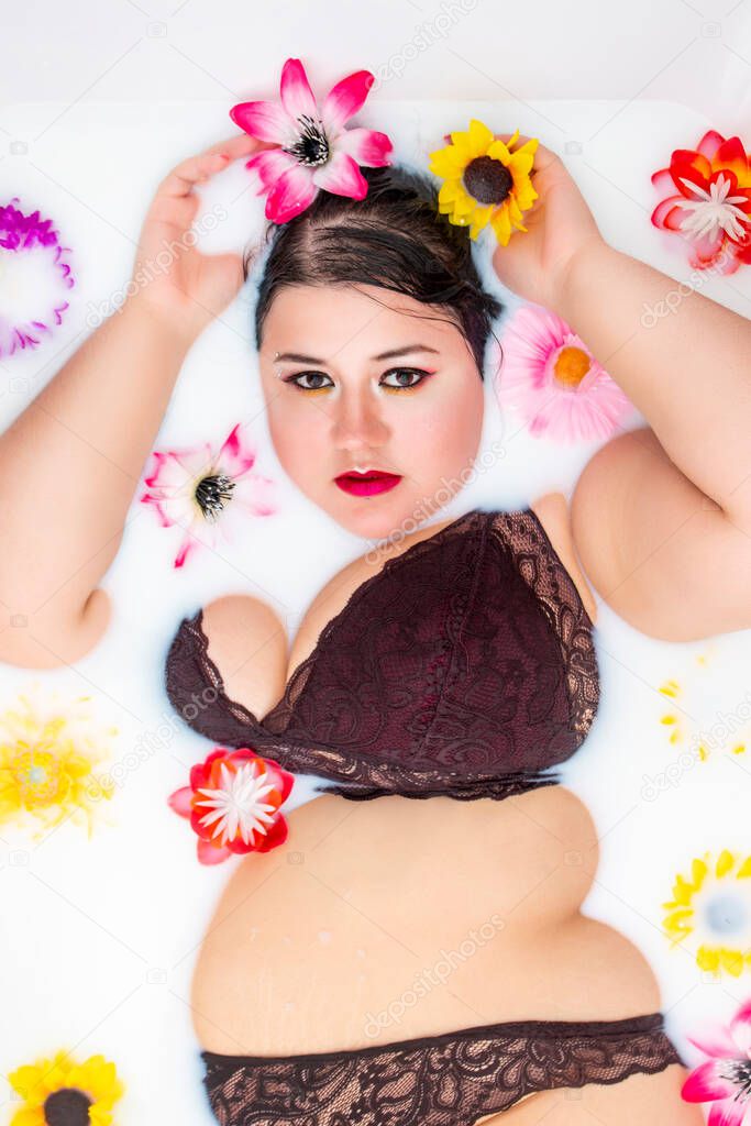 woman wearing sensual red lingerie on a milky bathtub with flowers.