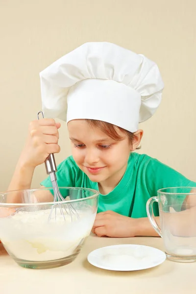 Little boy in chef hat shuffles dough for baking cake