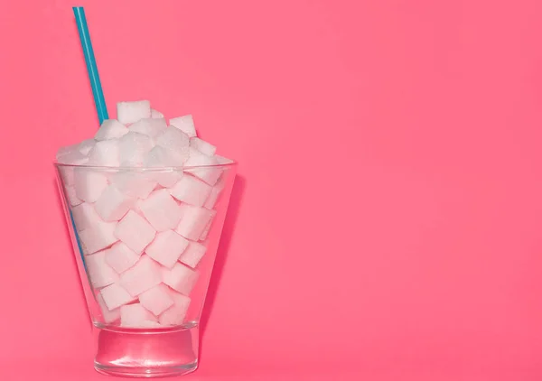 Glass with blue straw filled with sugar cubes on pink background. Junk food concept. — Stock Photo, Image