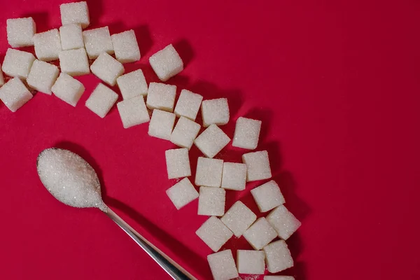 Ложка с сахаром на красный вон с кусочками сахара — стоковое фото