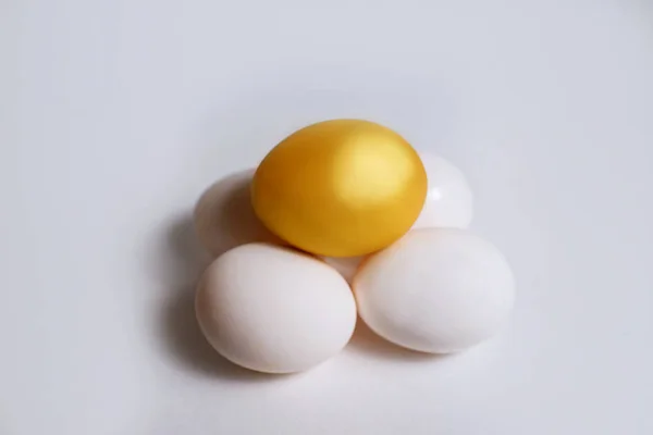 Złote jajko kurze leży na zwykłych białych jajach na białym tle — Zdjęcie stockowe