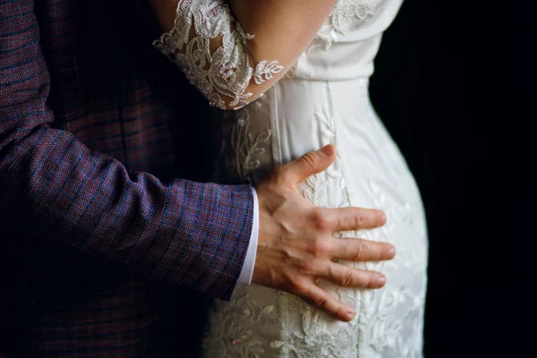 Bir erkek bir kadına belinden sarılır, damat ellerini gelinin kalçasından tutar.