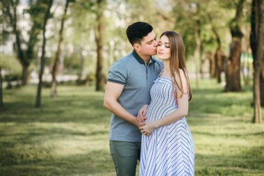 Genç hamile anne ve erkek arkadaşı parkta yürüyorlar, karı koca temiz havada yürüyorlar çocuğu bekliyorlar.