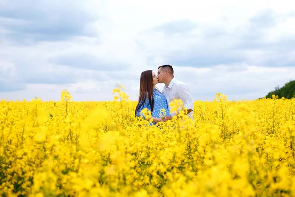 Una chica embarazada y su novio se paran en un campo de colza y disfrutan del clima primaveral, los futuros padres pasan tiempo al aire libre — Foto de Stock