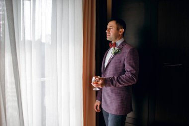 Adam elinde viski bardağıyla klasik bir ceket giymiş yakışıklı bir adam.