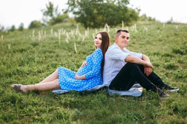 Evli bir çift çimenlerde oturmuş battaniye seriyor, hamile bir kız ve onun sevgili erkek arkadaşı