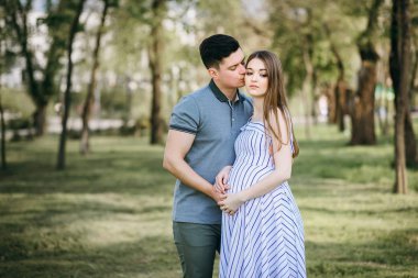 Genç hamile anne ve erkek arkadaşı parkta yürüyorlar, karı koca temiz havada yürüyorlar çocuğu bekliyorlar.