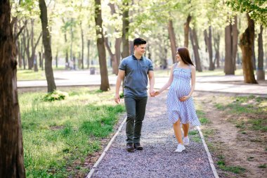 Genç hamile anne ve erkek arkadaşı parkta yürüyorlar, karı koca temiz havada yürüyorlar çocuğu bekliyorlar.