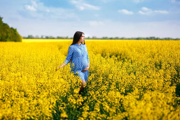 Beautiful pregnant girl walking on a rape field, stylish expectant mother in a blue dress — Stock Photo, Image