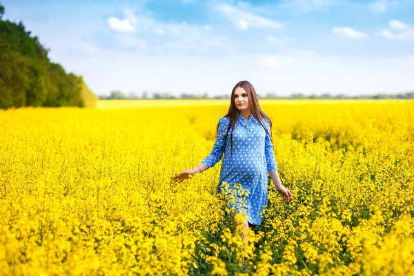 Beautiful pregnant girl walking on a rape field, stylish expectant mother in a blue dress — Stock Photo, Image