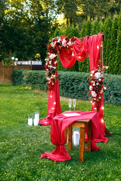 婚礼。仪式。婚礼拱门。公园里的绿草上矗立着鲜花和绿叶的红色婚礼拱门 — 图库照片