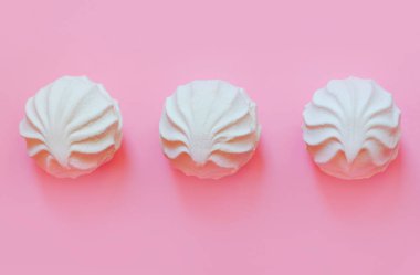 Pembe arka planda üç beyaz marşmelov, lezzetli bir tatlı.
