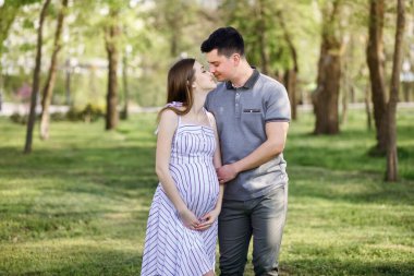 Genç hamile anne ve erkek arkadaşı parkta yürüyorlar, karı koca temiz havada yürüyorlar çocuğu bekliyorlar.
