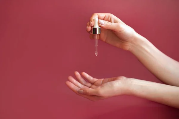 Ręce kobiet zbliżenie stosować olej ręczny na skórę z pipety, olej do ciała na różowym tle — Zdjęcie stockowe