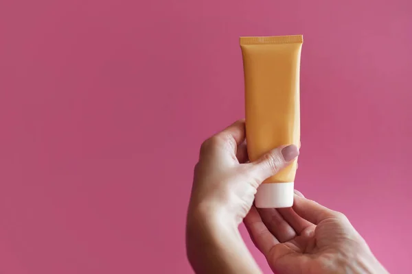 Woman holds hand cream, girl holds tube of cream on pink background