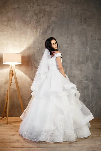 グレーの壁の背景に白いウェディングドレスの美しい花嫁、暖かい光の床ランプ — ストック写真