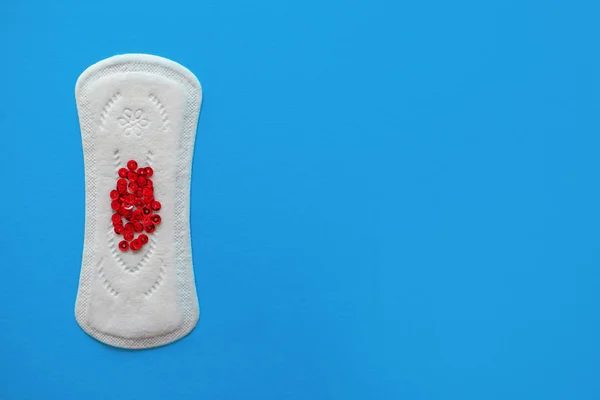 Menstrual pad with red sequins on a blue background, top view, miniature of the menstrual period — Stock Photo, Image