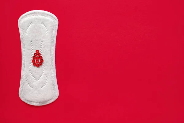 Менструальна подушечка з червоними блискітками у вигляді краплі крові на червоному тлі, вид зверху, мініатюра менструального періоду — стокове фото