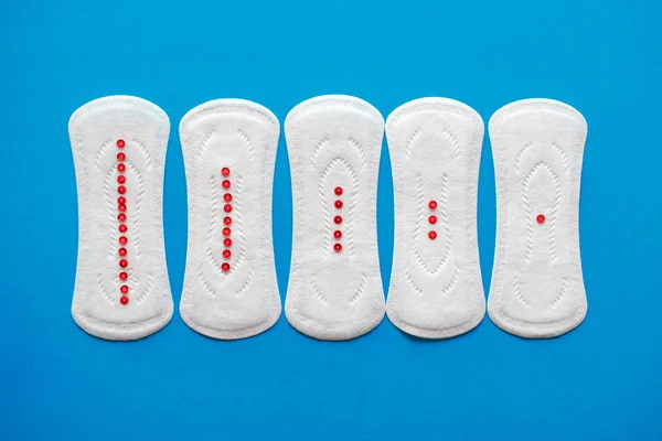 Five medical pads for women with red sparkles on a blue background, top view — Φωτογραφία Αρχείου