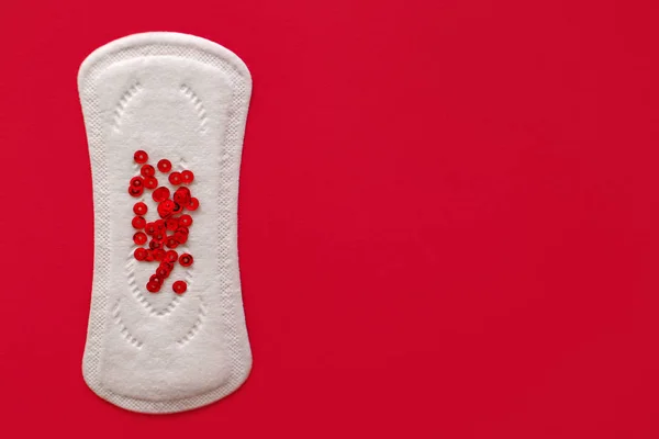 Menstrual pad with red sequins on a red background, top view, miniature of the menstrual period — Stock Fotó